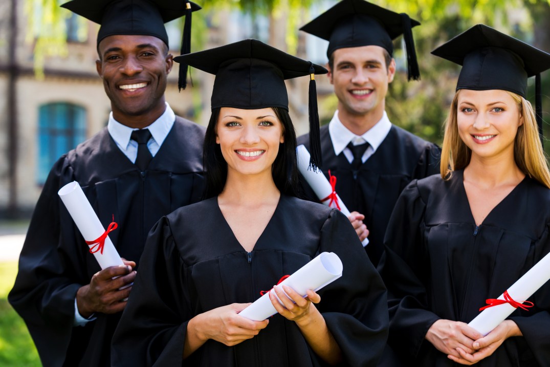 Feeling confident in their future. Four college graduates in graduation gowns standing close to each other and smiling
